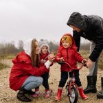 Happy family outdoors with children on a dirt path. Parents supporting kids on a bike ride.
